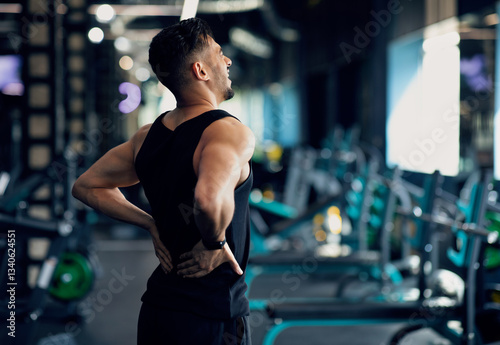 Fototapeta Naklejka Na Ścianę i Meble -  Portrait Of Young Arab Bodybuilder Suffering Lower Back Pain At Gym, Upset Middle Eastern Male Athlete Rubbing Painful Sore Zone After Getting Sport Injury, Having Lumbar Spine Ache, Copy Space