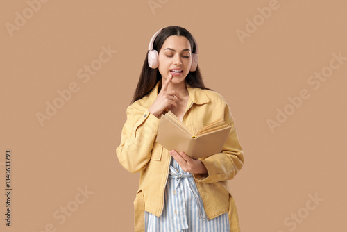 Beautiful young woman in headphones listening to audiobook and holding book o...