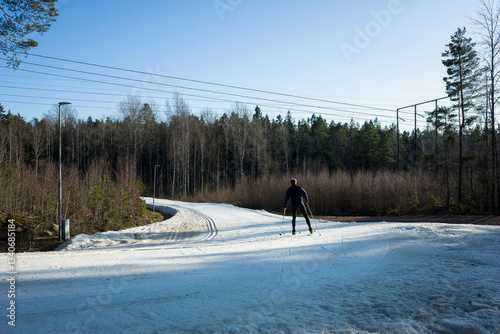 A skier moves along a winding artificial snow track in Rocklunda in Västerås, Sweden, in March. The bright white trail contrasts with the surrounding forest and bare trees under the spring sun