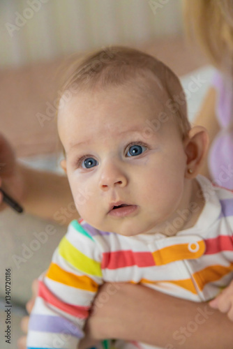 A young mother looks at her phone while her baby crawls on the bed next to her