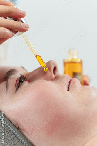 A beauty salon professional uses facial oil on a young female client. A drop close-up