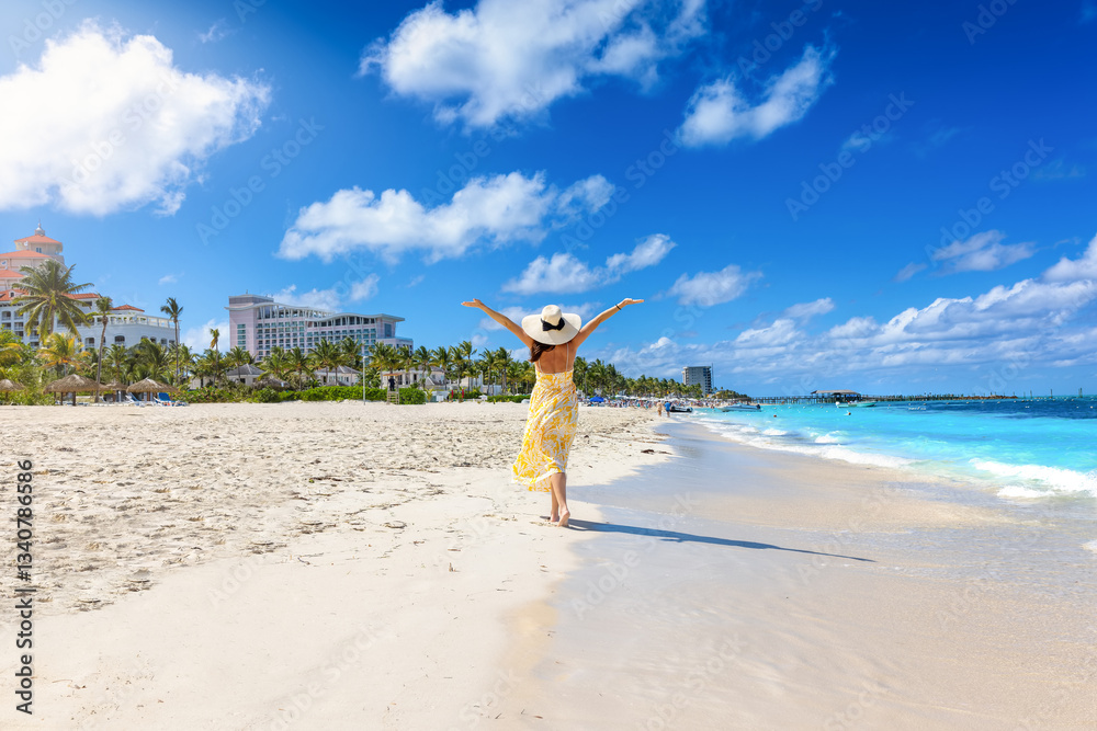 A happy holiday woman in a yellow summer dress walks down a tropical beach in Nassau, Bahamas, The Caribbean Sea