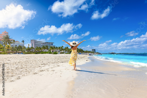 Obraz na płótnie A happy holiday woman in a yellow summer dress walks down a tropical beach in Nassau, Bahamas, The Caribbean Sea w salonie