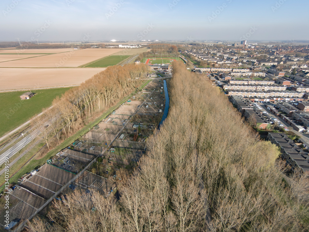 Aerial view of a rural area showcasing farmland, tree lines, and nearby residential neighborhoods in clear weather