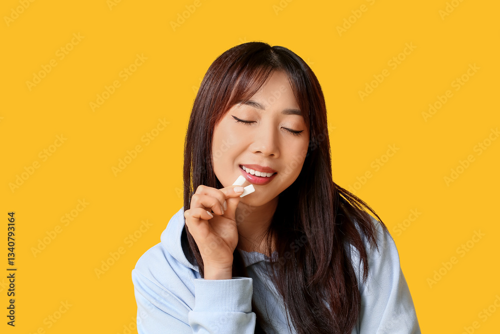 Fototapeta premium Pretty young Asian woman with chewing gums on yellow background