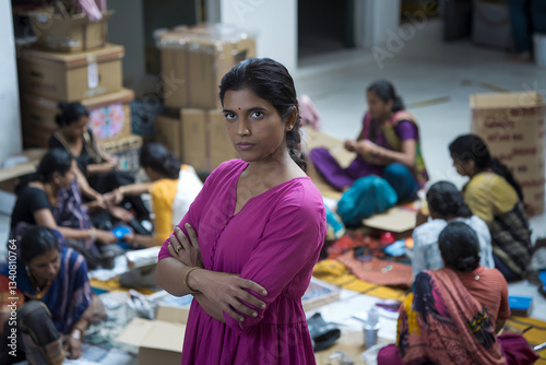 a determined woman stands with her arms crossed, surveying her team at work. She is surrounded by colleagues who are focused on their tasks