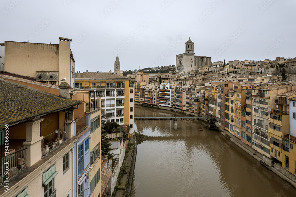 Girona city, view over the Onyar river with the hanging houses over the banks and the Cathedral at the background, during a cold, overcast winter day.