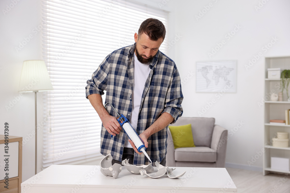 Man with caulking gun glueing pieces of ceramic piggy bank indoors