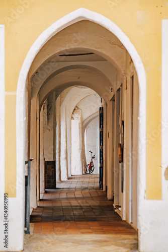 Obraz na płótnie Explore the hidden charm of Ciutadella with this image of an arched passage, featuring architectural arches, a tiled floor, and a distant bicycle. Ideal for travel, culture, and architectural themes w salonie