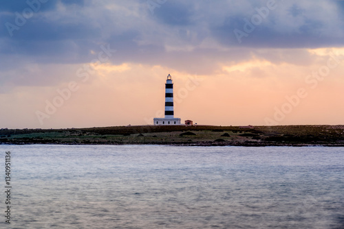 Obraz na płótnie Capture the iconic beauty of Minorca with this image of a black and white lighthouse in the distance, set against twilight skies and a serene sea. Perfect for travel, nature, and scenic themes w salonie