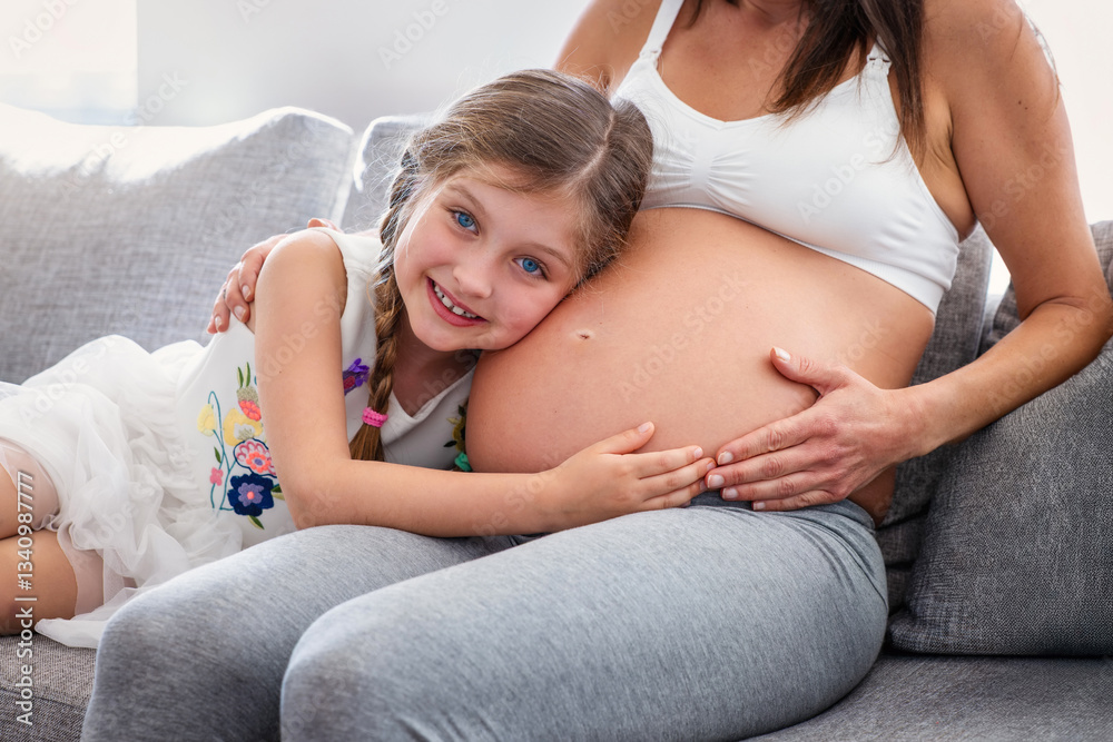 A cute girl listens to the belly of her pregnant mother in anticipation of her sibling
