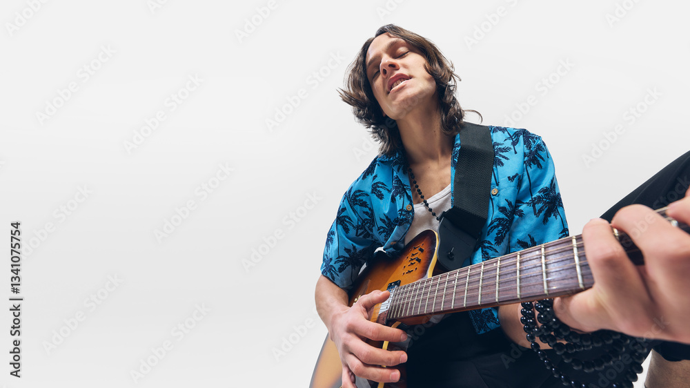 Young man, guitarist in tropical shirt strumming melody with closed eyes, deeply connected to music, playing guitar on white background. Concept of music, festival, performance, concert, rock, talent Young man, guitarist in tropical shirt strumming melody with closed eyes, deeply connected to music, playing guitar on white background. Concept of music, festival, performance, concert, rock, talent