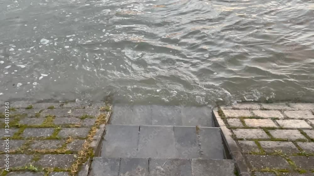 Treppenstufen am Rhein, die bei Hochwasser und Sonnenuntergang mit Wellen in der Strömung zu sehen sind