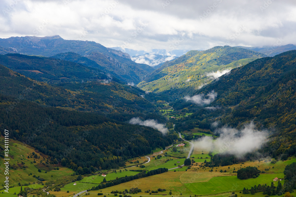 Obraz premium Valle verde rodeado de montañas y niebla, visto desde el alto de Larra-Belagua, Navarra, España