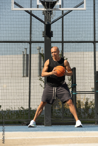 Obraz na płótnie Basketball player with orange basketball ball on sports court at courtyard. Street style. Streetball player. Game moment. w salonie