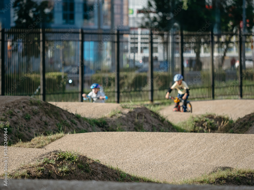 Fototapeta premium Dirt bike trail and child on bike at background. Pump track made from soil and sand for extreme sport bmx race. Bicycling in urban landscape