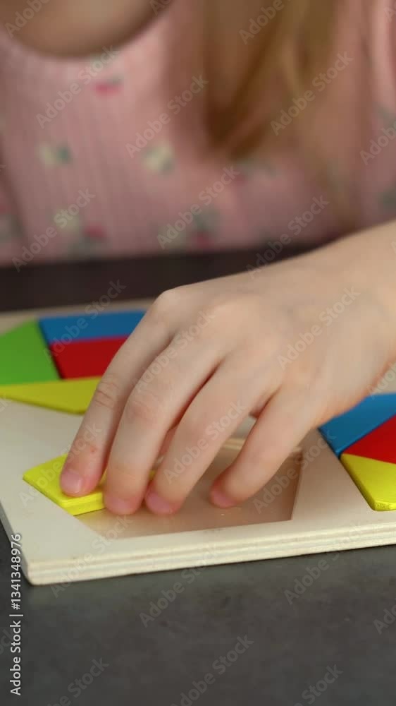 Close up of childs hands put colored tangram puzzle. Family spends leisure time put wooden jigsaw. Education concept. Vertical shot