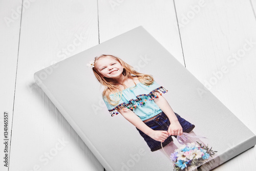 stretched canvas print with gallery wrapping, featuring a smiling young girl in a blue top and denim shorts holding a floral bouquet. The canvas rests on a white wooden surface at an angle