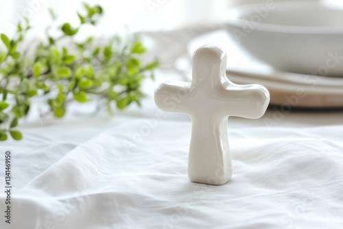White Ceramic Cross on Light Tablecloth Surrounded by Greenery and Dishes in Soft Natural Light