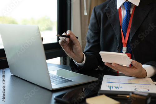 A man in a suit is looking at a piece of paper with graphs on it. He is holding a pen and he is analyzing the data. The scene suggests a professional setting


