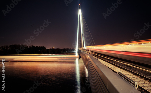 Long exposure image of subway driving along the bridge. Blurred motion of train driving at speed away from camera at night, ship passing under the bridge.