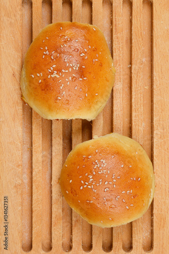 Two homemade hamburger buns sprinkled with sesame seeds lie on a wooden cutting board