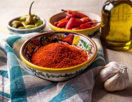 Portuguese ceramic bowls filled with colorful piri-piri peppers resting on a cloth beside garlic and olive oil bottles