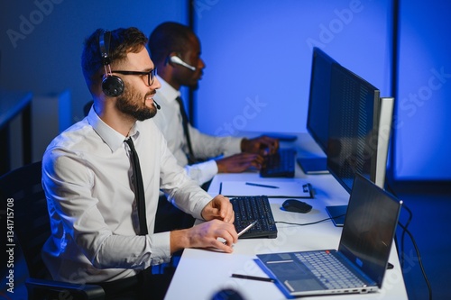 Happy Confident Technical Customer Support Specialist Having a Headset Call in a Monitoring and Control Room Filled with Colleagues and Display Screens