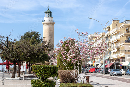 Fototapeta Naklejka Na Ścianę i Meble -  Spring period in the streets of Alexandroupolis Evros Greece, pink magnolia flowers near the Lighthouse, Greek English translation sign from the municipality, seaport and blue sky