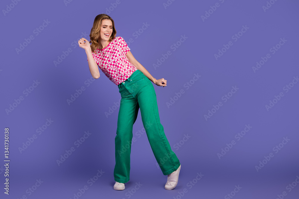 Obraz premium Stylish young woman in vibrant colorful attire dancing joyfully against a purple background.