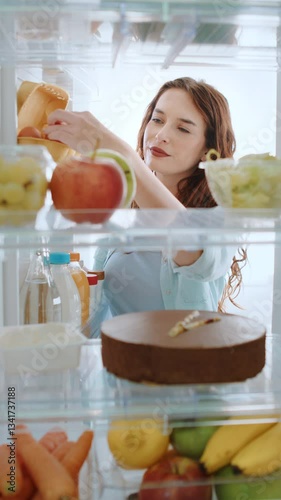 Beautiful young woman opens fridge door, takes out a egg, preparing healthy breakfast meal using fresh groceries. Point of View POV shot from inside a kitchen refrigerator full of healthy food