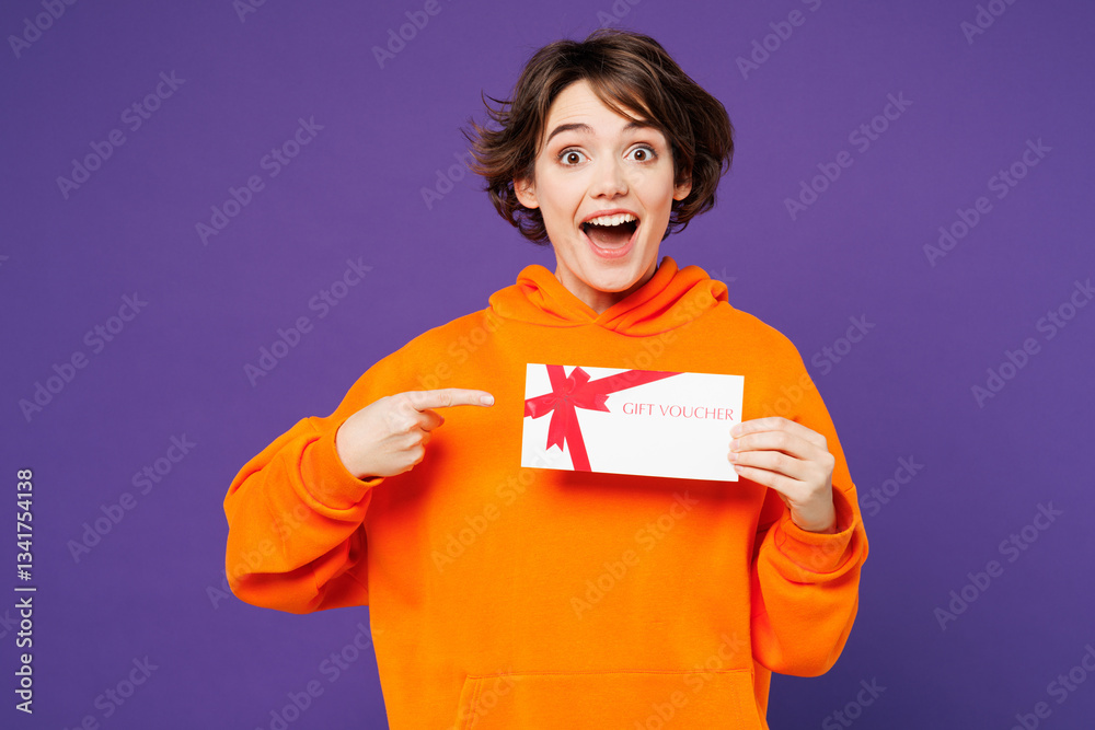Fototapeta premium Young smiling happy woman wear orange hoody casual clothes hold point finger on gift certificate coupon voucher card for store isolated on plain purple background studio portrait. Lifestyle concept.