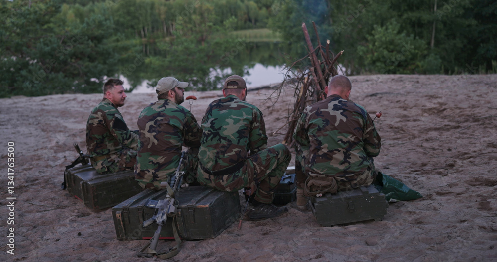 Fototapeta premium Hunters relax by the lake after a successful game hunt, grilling sausages over a bonfire, while their weapons are safely leaned against boxes behind them.
