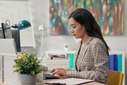 Attractive, experienced secretary of company is sitting in office in front of computer tapping fingers on keyboard writing messages emails filling out documents reports preparing protocols for manager