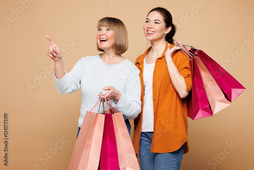 Elder parent mom with young adult daughter two women together wear casual clothes hold shopping package bags point aside isolated on plain beige background. Family, Black Friday sale buy day concept. photo