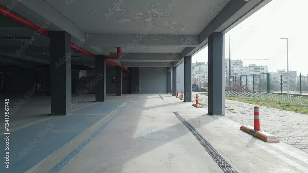 A drone captures an empty underground parking garage with concrete pillars and open sides. The industrial space is illuminated by natural light, creating a modern yet abandoned atmosphere A drone captures an empty underground parking garage with concrete pillars and open sides. The industrial space is illuminated by natural light, creating a modern yet abandoned atmosphere