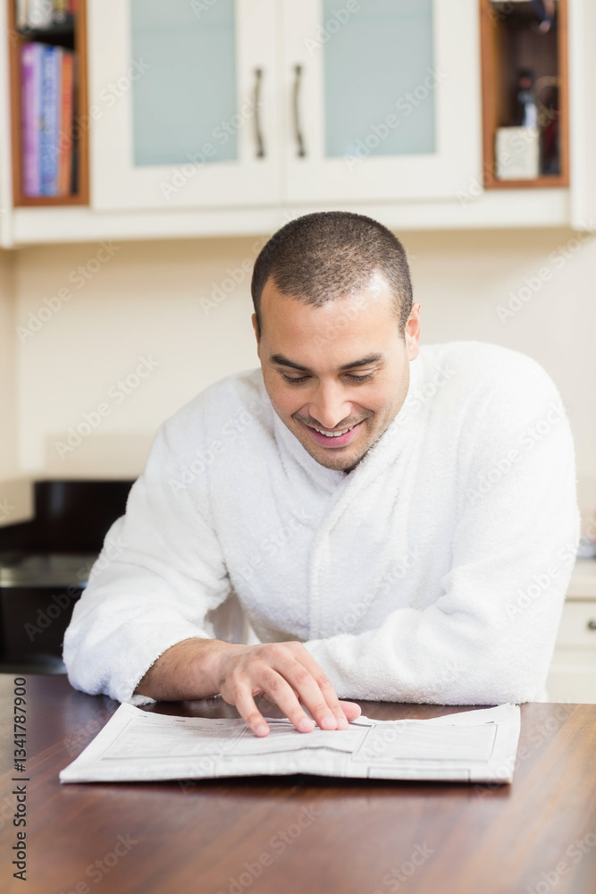 Smiling man in bathrobe reading newspaper at kitchen table, enjoying morning Smiling man in bathrobe reading newspaper at kitchen table, enjoying morning