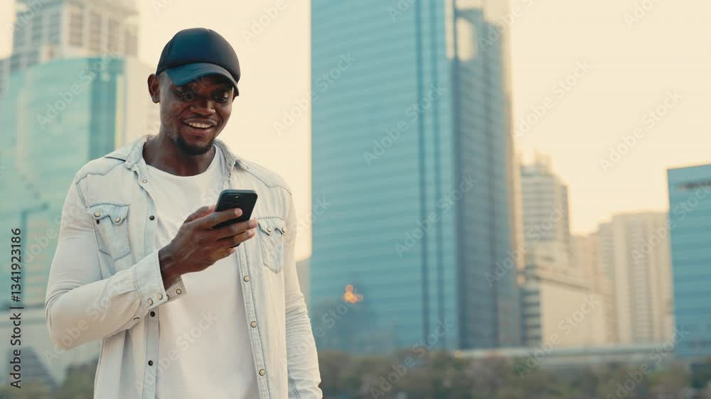 Portrait of happy African American man with cellphone showing winner gesture against skyscrapers. Guy gets good news via mobile phone screen on street. Urban lifestyle Portrait of happy African American man with cellphone showing winner gesture against skyscrapers. Guy gets good news via mobile phone screen on street. Urban lifestyle