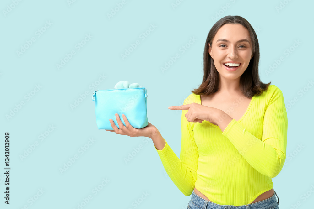 Beautiful young woman with cosmetic bag full of makeup products pointing at something on blue background Beautiful young woman with cosmetic bag full of makeup products pointing at something on blue background