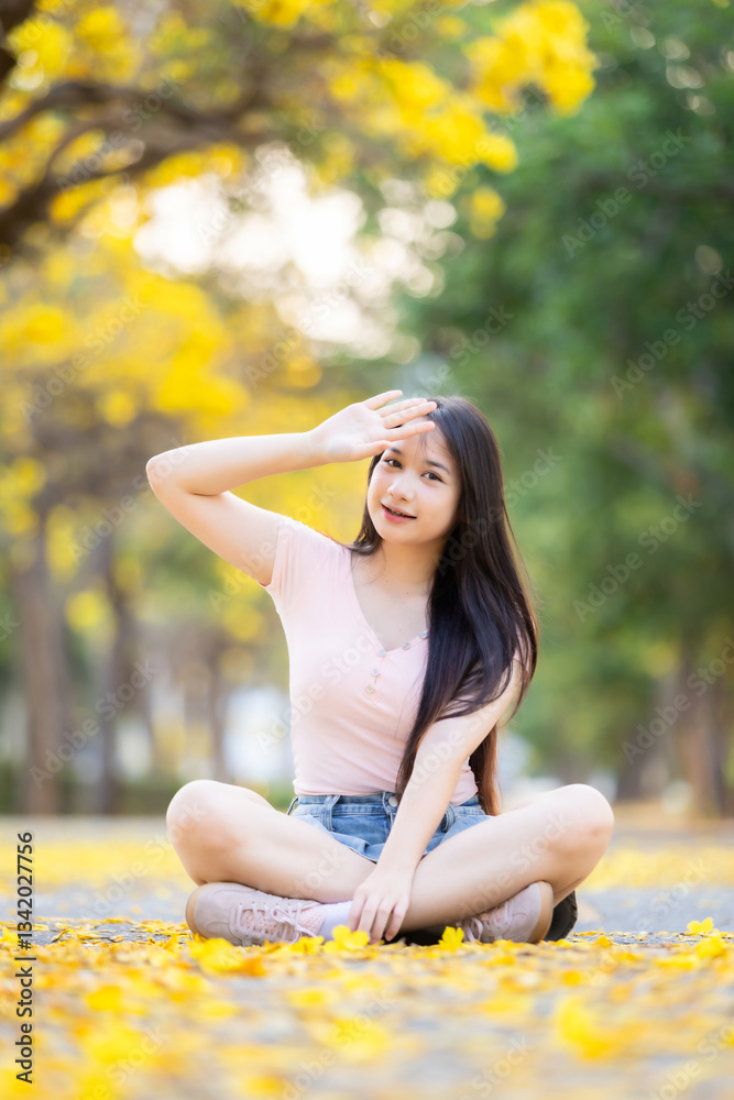 Portrait cute smiles Asian of attractive young teenage girl in Beautiful blooming Yellow Golden Tabebuia Chrysotricha flowers with the park in spring day at Evening background in Thailand.
