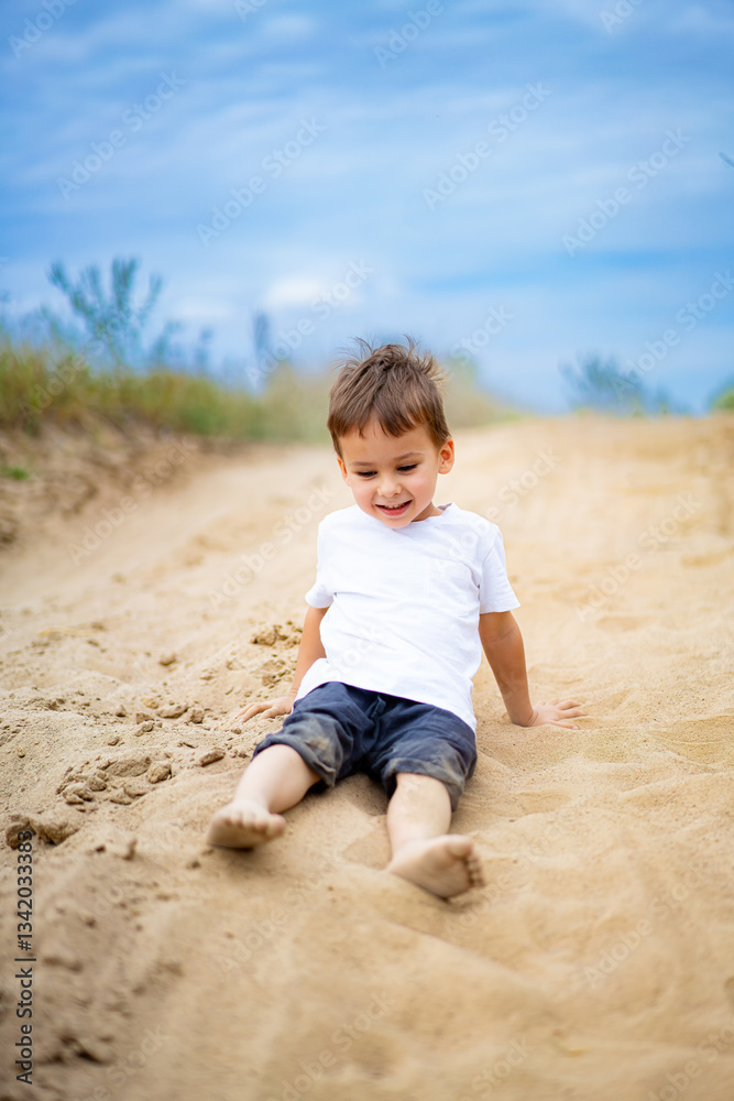 Child enjoys sandy playtime on trail. A young boy plays joyfully in the sand along a dirt trail under a cloudy sky, smiling and having fun. Child enjoys sandy playtime on trail. A young boy plays joyfully in the sand along a dirt trail under a cloudy sky, smiling and having fun.