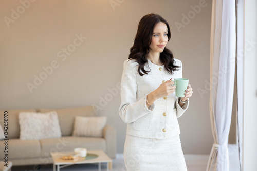 Stunning woman in a fitted suit gracefully holds a cup of coffee, symbolizing sophistication and mindfulness in a professional space.
