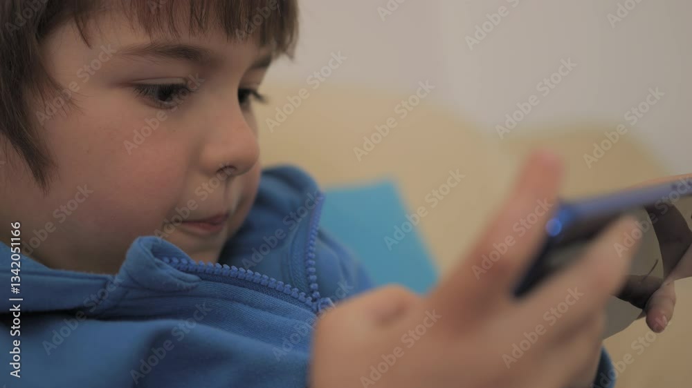 Closeup Child Playing Games In Phone at Home on Couch. Boy Playing Video Game on Mobile Phone. Preschooler Plays Video Game Smartphone on Sofa. Kid Using Phone for Gaming Online Education Social Media Closeup Child Playing Games In Phone at Home on Couch. Boy Playing Video Game on Mobile Phone. Preschooler Plays Video Game Smartphone on Sofa. Kid Using Phone for Gaming Online Education Social Media