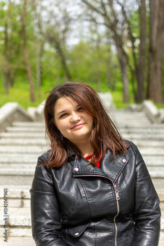 A woman in a stylish black leather jacket sits on stairs