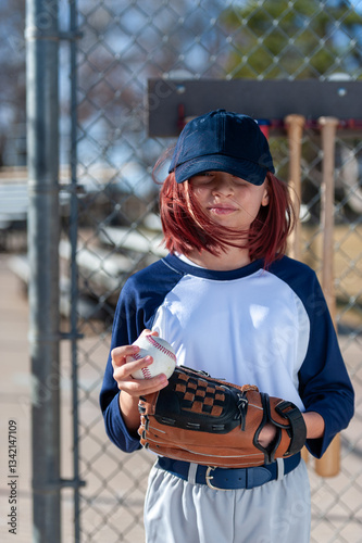 Young girl in little league baseball uniform with glove and ball in dugout