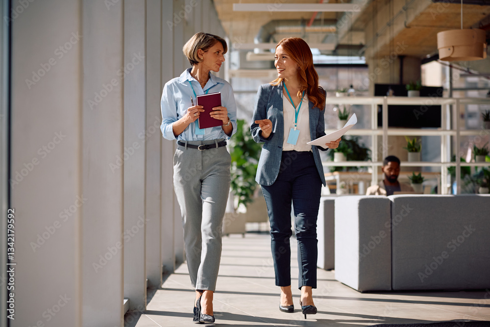 Fototapeta premium Smiling female entrepreneurs communicating while walking through office.