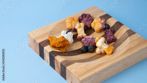 Frozen dog treats made with colorful blueberries, pumpkin, yogurt, and coconut oil, in a unique wooden bowl, healthy organic pet snack.