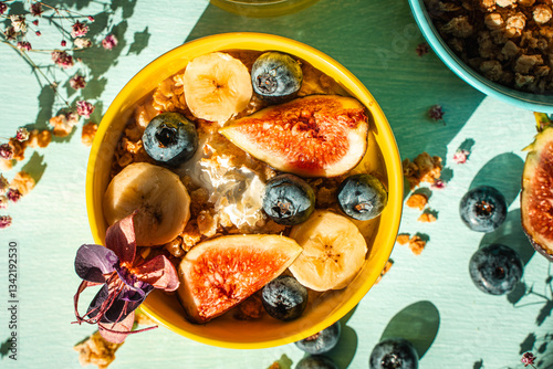 Healthy breakfast, figs, bananas and blueberries in yellow and blue bowls with yogurt and granola on a light table. View from above.