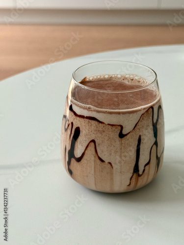 A close-up view of a glass filled with a creamy coffee-milk drink or cocoa, with smooth gradient chocolate cyrop streaks, on a white table, elegant composition