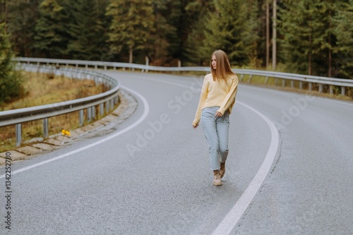Wallpaper Mural A young woman strolls confidently along a winding road, dressed in a cozy yellow sweater and light jeans, with trees framing the tranquil scene. Torontodigital.ca